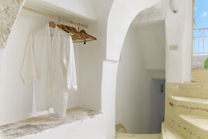 A white-walled room with a wooden hanger holding white garments. A staircase with a yellow railing leads to an outdoor balcony.
