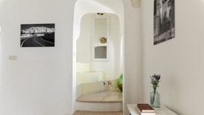 Una scala con un muro bianco, una fotografia incorniciata, un vaso con fiori e un libro su un tavolino in legno.