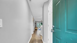 A hallway with a wooden floor, white walls, and a teal door.