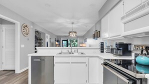 A modern kitchen with white cabinetry, a built-in dishwasher, a large island with a sink, and a coffee machine.