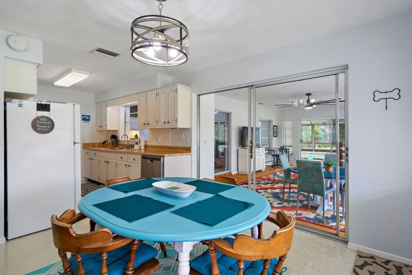 Cocina moderna con armarios blancos, una isla central y un área de comedor con una mesa redonda y sillas azules.