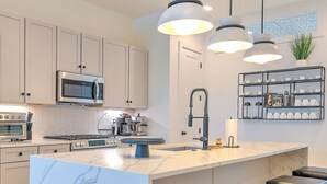 A modern kitchen with white cabinets, a stainless steel microwave, a gas stove, and a marble island with bar stools. - Rooftop Hot Tub 13 Beds Game Room (Nashville)