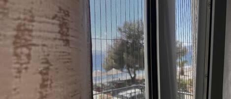 A window with a metal screen, a concrete wall, and a view of a street with parked cars and trees.