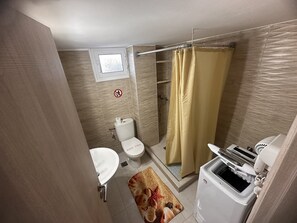 Ein kleines Badezimmer mit Toilette, Waschbecken, Dusche und einer kleinen Waschmaschine.