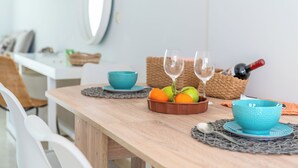 Une table de salle à manger en bois, sur laquelle se trouve un saladier rempli de fruits, deux verres à vin et une bouteille de vin.