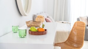 Une table à manger avec un saladier rempli de pommes et d’oranges, deux verres verts et un panier en osier.