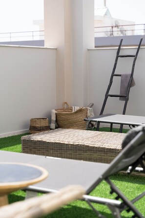 A balcony with a wicker sofa, a small round table, and a ladder. - Alpha Urban Suites (Rhodes)