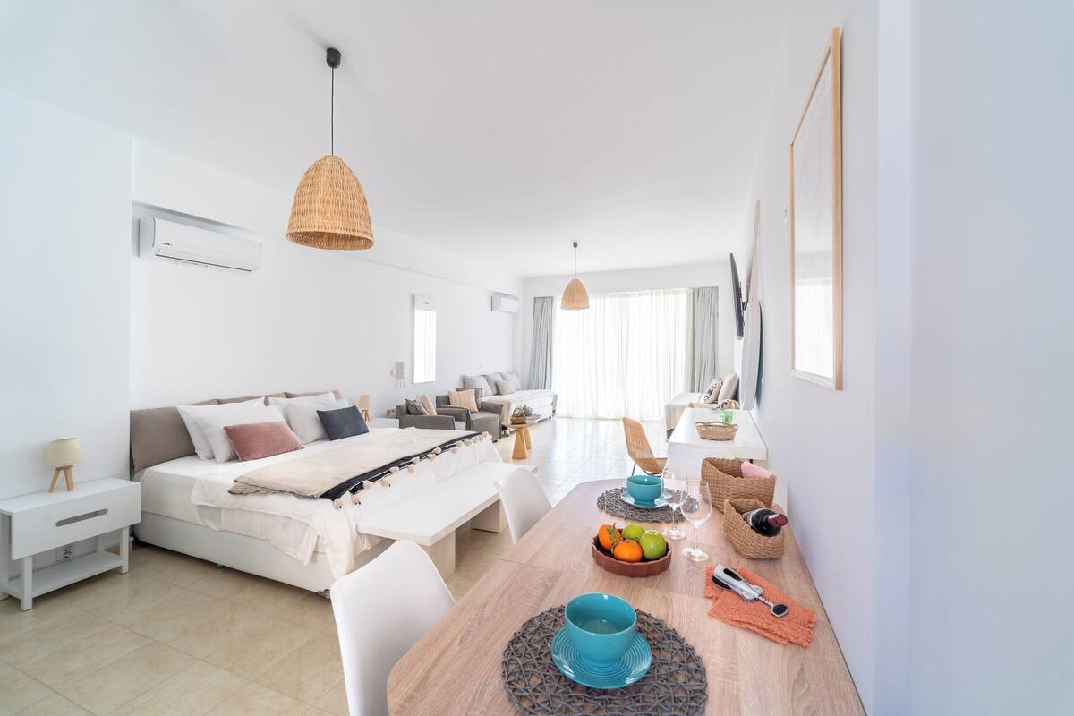 Un dormitorio moderno y bien iluminado con una cama grande, mesitas de noche y una zona de comedor con una mesa preparada para dos.