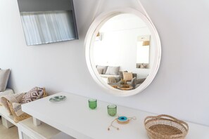 A modern living room with a white sofa, a round mirror, and a white console table with decorative items. - Alpha Urban Suites (Rhodes)