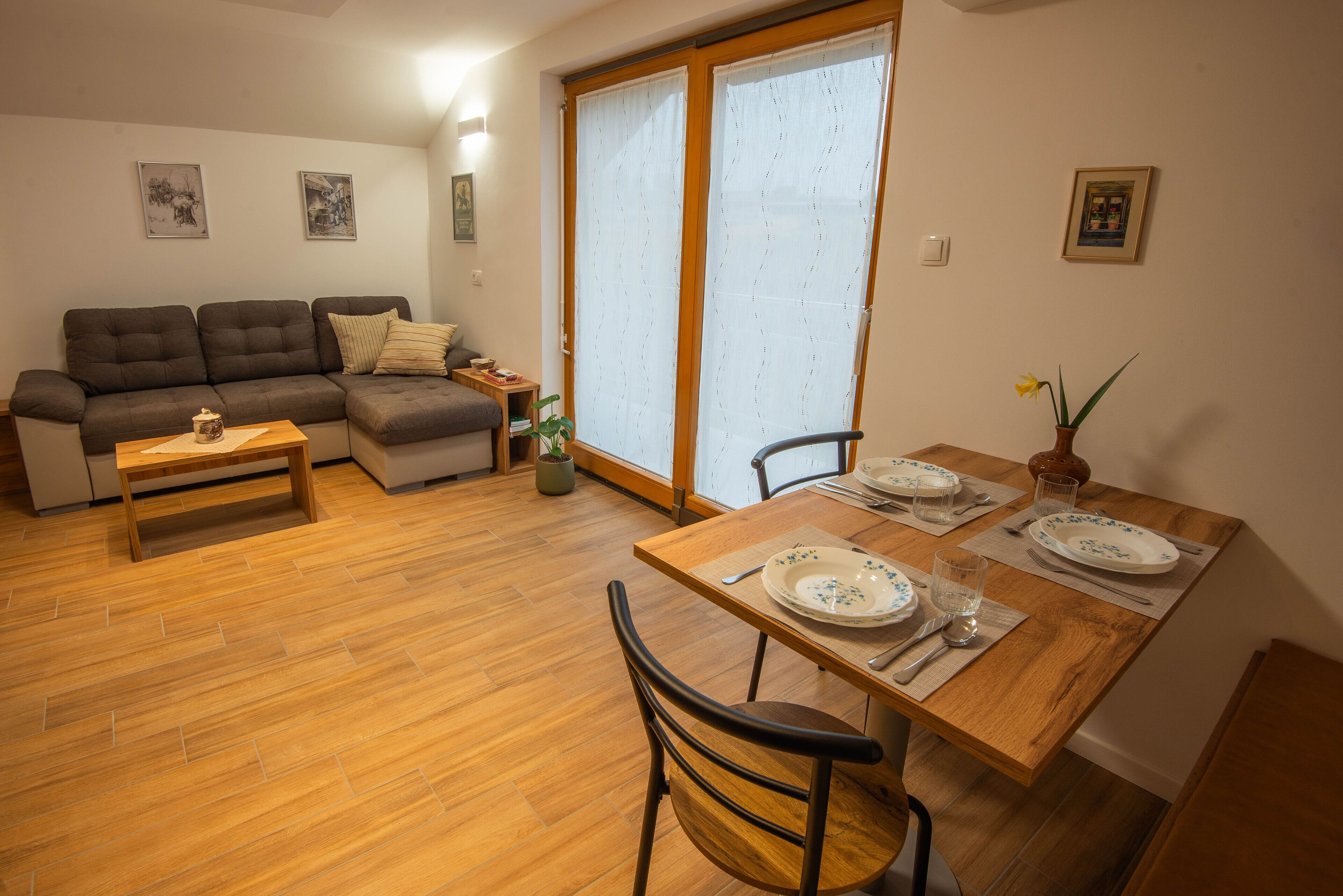 Ein gemütliches Wohnzimmer mit einer Couch, einem Esstisch für zwei Personen und einem großen Fenster mit Vorhängen.