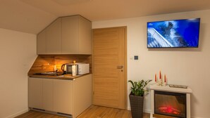 Eine kompakte Küche mit Mikrowelle, Toaster und Holzschränken. Ein Fernseher ist an der Wand angebracht, und ein Kamin mit Kerzen ist sichtbar.
