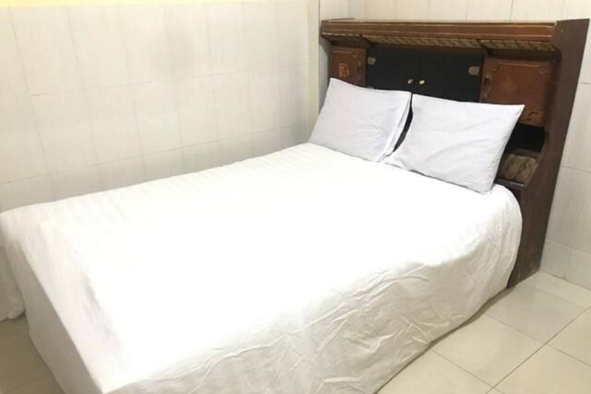 A neatly made bed with white linens in a room with a wooden headboard and tiled floor.