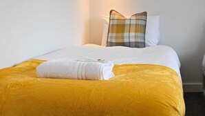A neatly made bed with a yellow bedspread and white pillows, including a plaid one. - Dings: Central Bristol House by STAE-Homes (Bristol City)