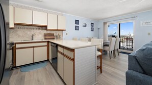 A compact kitchen with a dining area, a balcony with a view, and a small living space. - Sunchaser 407 - 2br/2baths at 36th St, steps to beach, elevator &2 car parking (Ocean City)