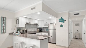A modern kitchen with white cabinetry, a granite countertop, and a central island with stools.