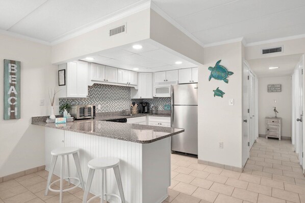 A modern kitchen with white cabinetry, a granite countertop, and a central island with stools.
