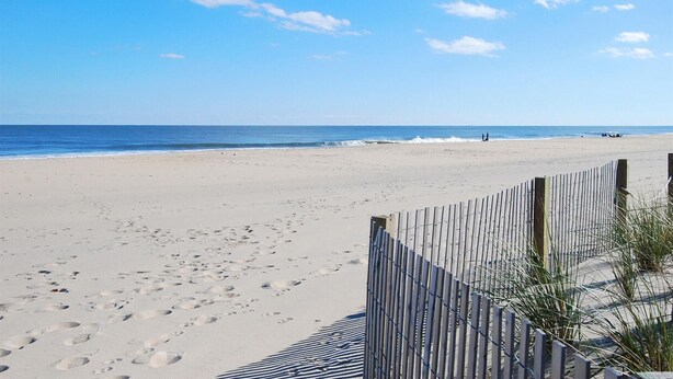 A beach with a wooden fence and footprints in the sand.