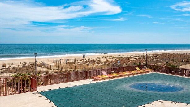 A beach view with a fenced pool area and lounge chairs. - Oceanfront for 9 people at the Rainbow / outdoor pool (Ocean City)