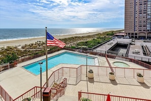 A rooftop pool with a view of the beach and ocean, a flagpole with an American flag, and a high-rise building in the background. - Oceanfront for 9 people at the Rainbow / outdoor pool (Ocean City)