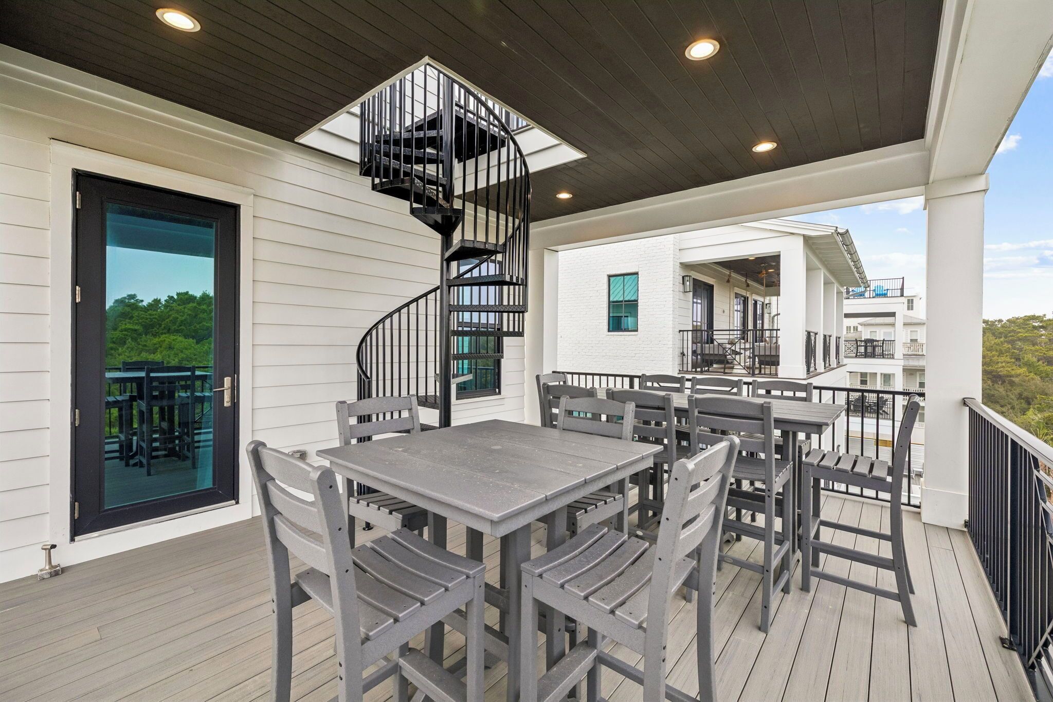 A covered outdoor area with a spiral staircase, a dining table with chairs, and a view of the surrounding buildings.