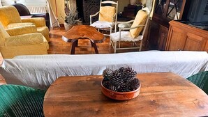 Een houten tafel met een dennenappel als decoratie, een groene geweven stoel en een witte bank in een gezellige woonkamer.
