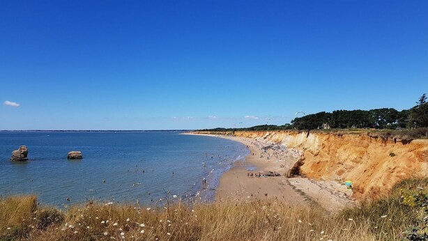 Een strand met helderblauw water, een zandstrand en een klif begroeid met vegetatie.
