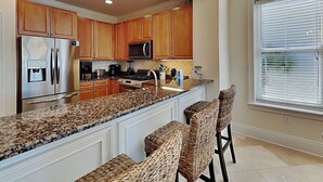 A kitchen with wooden cabinets, stainless steel appliances, a granite countertop, and wicker bar stools.