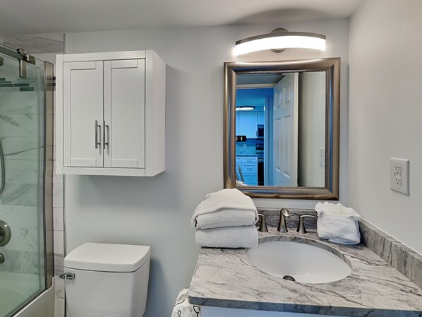 Un baño con inodoro blanco, lavamanos de mármol y cabina de ducha de vidrio.