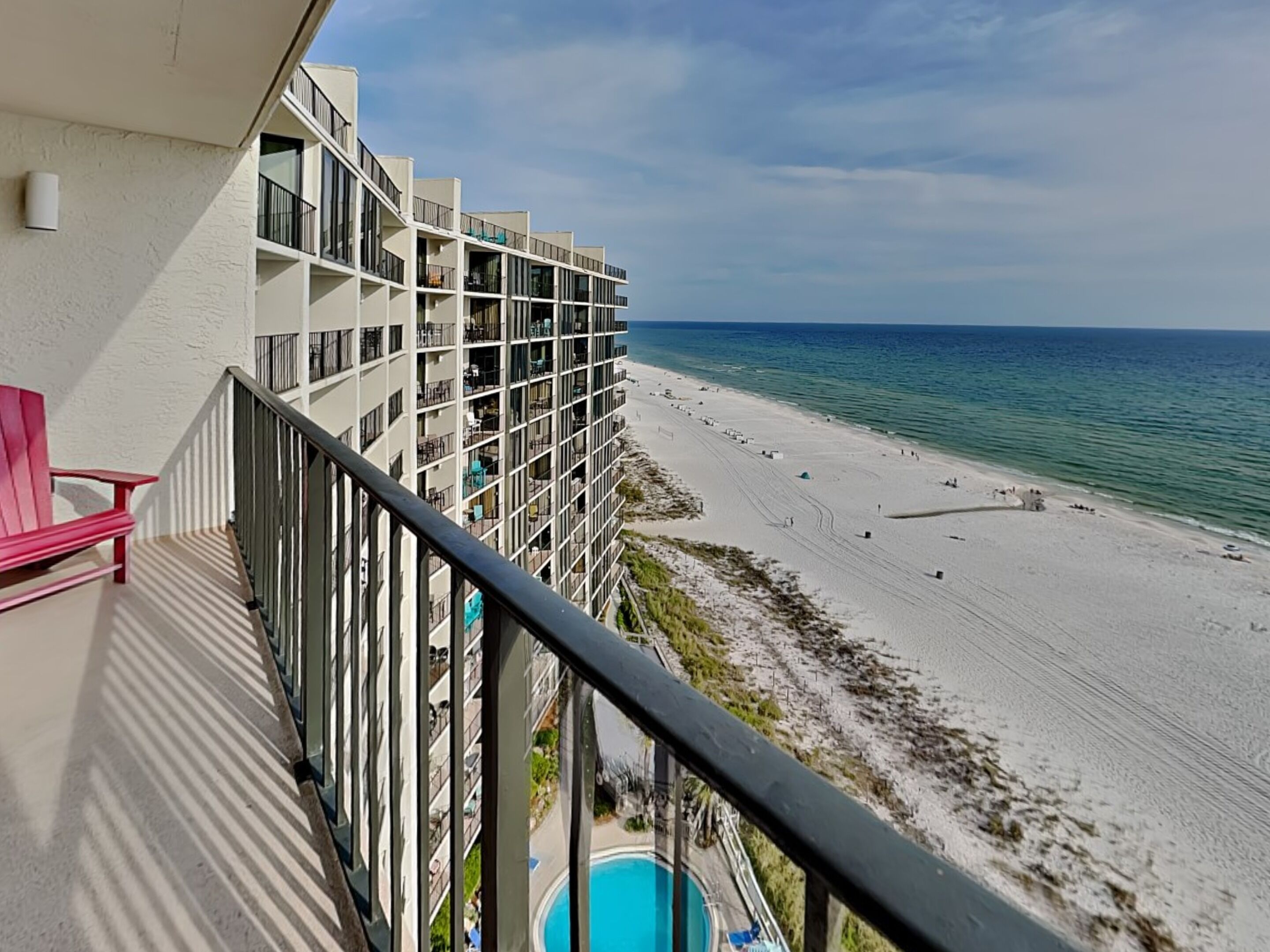 A hotel with a pool, beach view, and a red chair on the balcony.
