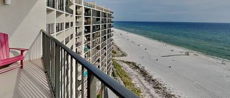 Hotel com piscina, vista para a praia e uma cadeira vermelha na varanda.