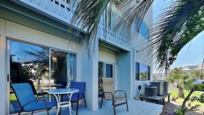 A covered outdoor area with a table and chairs, a bench, and a small garden with a palm tree. - Island Home #102 | Close to Beach and Destin Harbor (Destin)