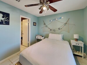 A bedroom with a bed, a ceiling fan, a 'NO WAKE ZONE' sign, a nightstand, and a door leading to another room.