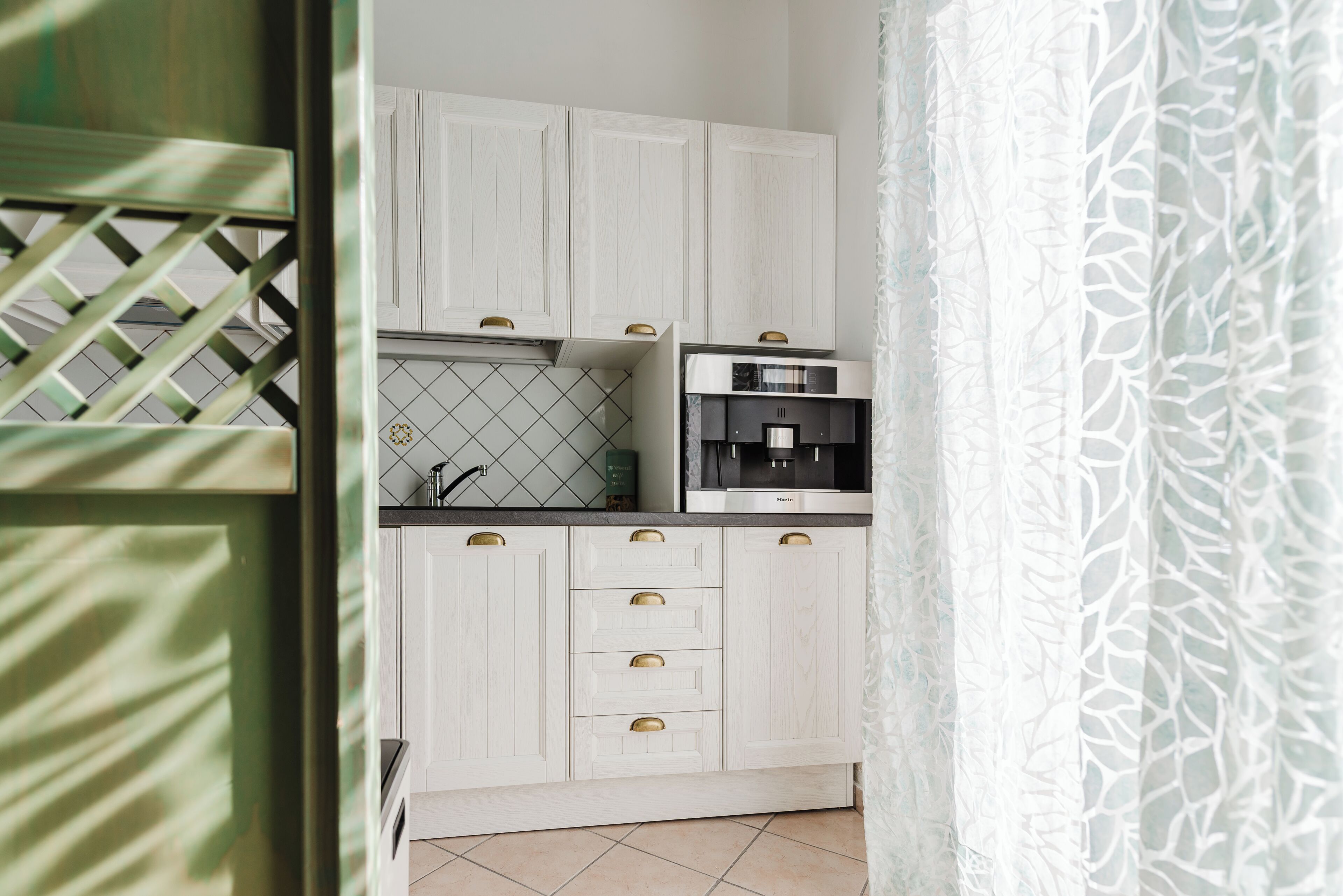 Una cocina con armarios blancos, una cafetera y un salpicadero de azulejos.
