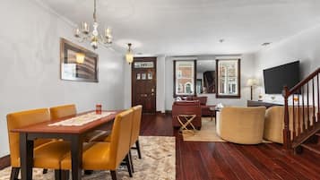 A dining area with a wooden table and chairs, a chandelier, and a framed picture on the wall.
