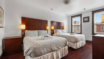 A hotel room with two beds, wooden headboards, bedside lamps, a dresser, and a window with blinds.