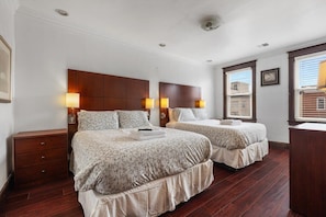 A hotel room with two beds, wooden headboards, bedside lamps, a dresser, and a window with blinds.