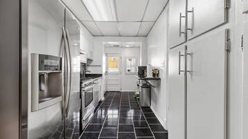 A narrow kitchen with stainless steel appliances, white cabinets, and black tiled flooring.