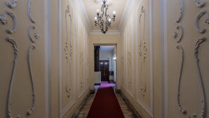 Un couloir agrémenté de décorations murales élaborées, d’un lustre et d’une moquette rouge.