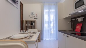 Une cuisine de taille réduite avec un coin repas, une horloge au mur et une fenêtre ornée de rideaux légers.