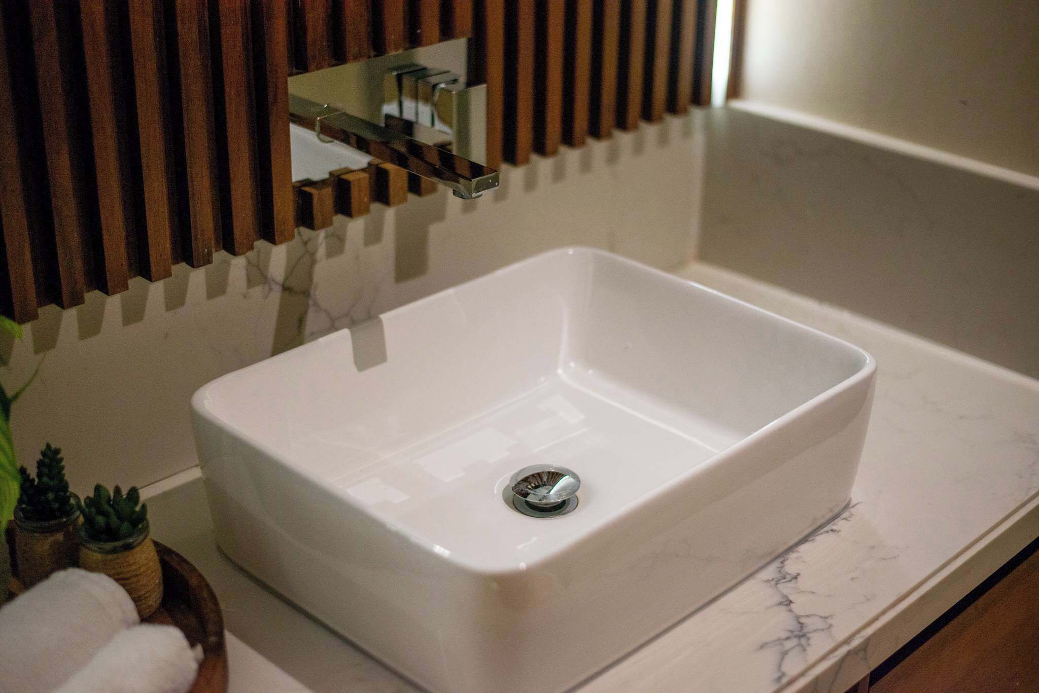 Un lavamanos blanco rectangular con un grifo de cromo, una encimera de mármol y una pequeña planta en maceta a un lado.