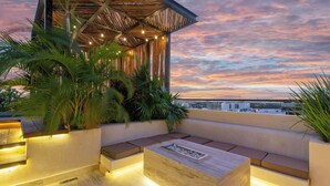 Une terrasse sur le toit, aménagée avec un espace salon, des plantes et offrant une vue sur le paysage urbain au coucher du soleil.