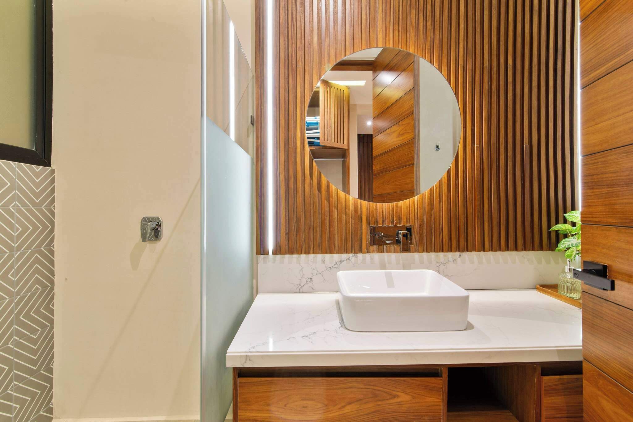 Une salle de bain avec un meuble-lavabo en bois, un lavabo blanc et un miroir doté d’un cadre circulaire.