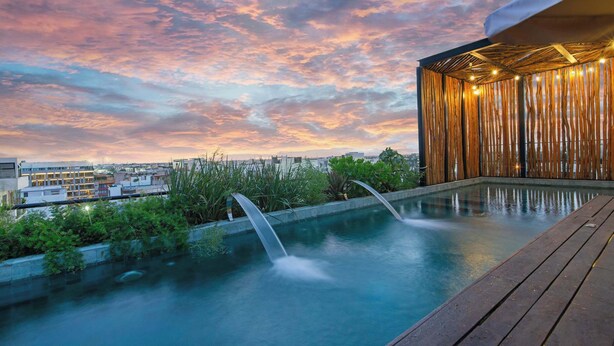 Une piscine sur le toit, agrémentée d’une cascade, entourée d’une végétation luxuriante et dotée d’une terrasse en bois.