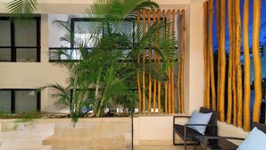 Un espace extérieur moderne, aménagé avec une balustrade en verre, un palmier et un mur en bambou.