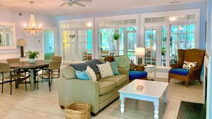 A spacious living room with a sofa, chairs, a dining table, and large windows.
