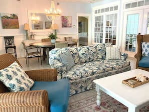 A living room with a patterned sofa, wicker chairs, a dining table, and a chandelier. - Melrose Oasis cottage by the Sea (Daufuskie Island)