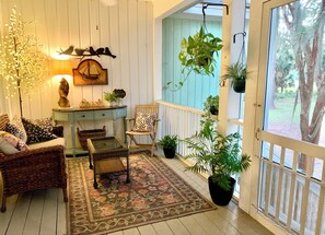 A cozy room with a wicker sofa, a wooden chair, a small table, a decorative wall, and a view through a screened door.