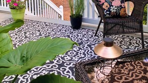 A deck with a wicker chair, a potted plant, and a lamp.