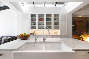 A modern kitchen with a white countertop, a double sink, and a skylight above.