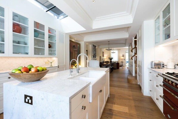 A spacious kitchen with white cabinetry, a marble countertop, and a large island with a bowl of fruit.